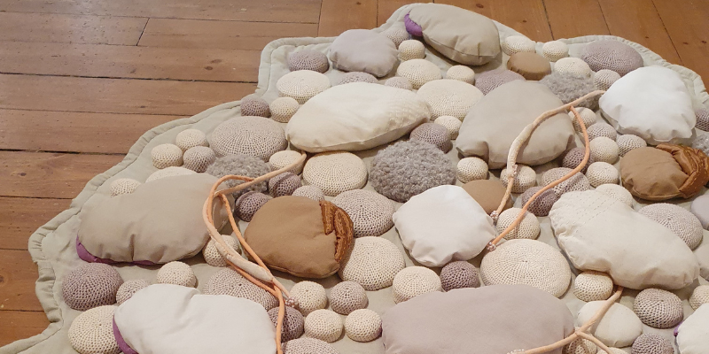 An artwork depicting rocks made of brown and gray fabrics on a wooden floor.